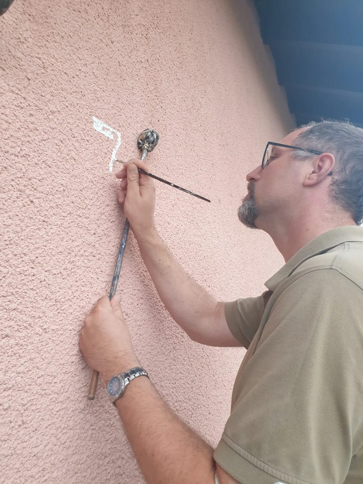 Maler von Maler-Gebert bessert eine strukturierte rosa Fassade mit Pinsel und Spachtel sorgfältig aus